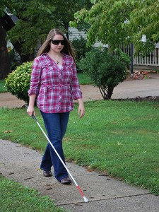 Colleen walking with cane and sunglasses