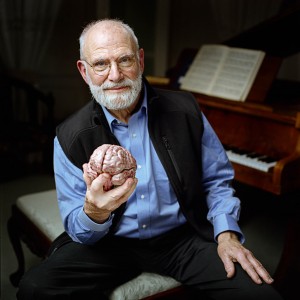 Dr. Oliver Sacks holding a model of a brain and sitting by a piano