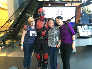 Alyssa, Colleen, and Cheryl pose with a someone dressed as Deadpool, who holds a sword near their throats