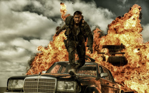 Tom Hardy as Mad Max nearly consumed by an explosion of fire and car parts